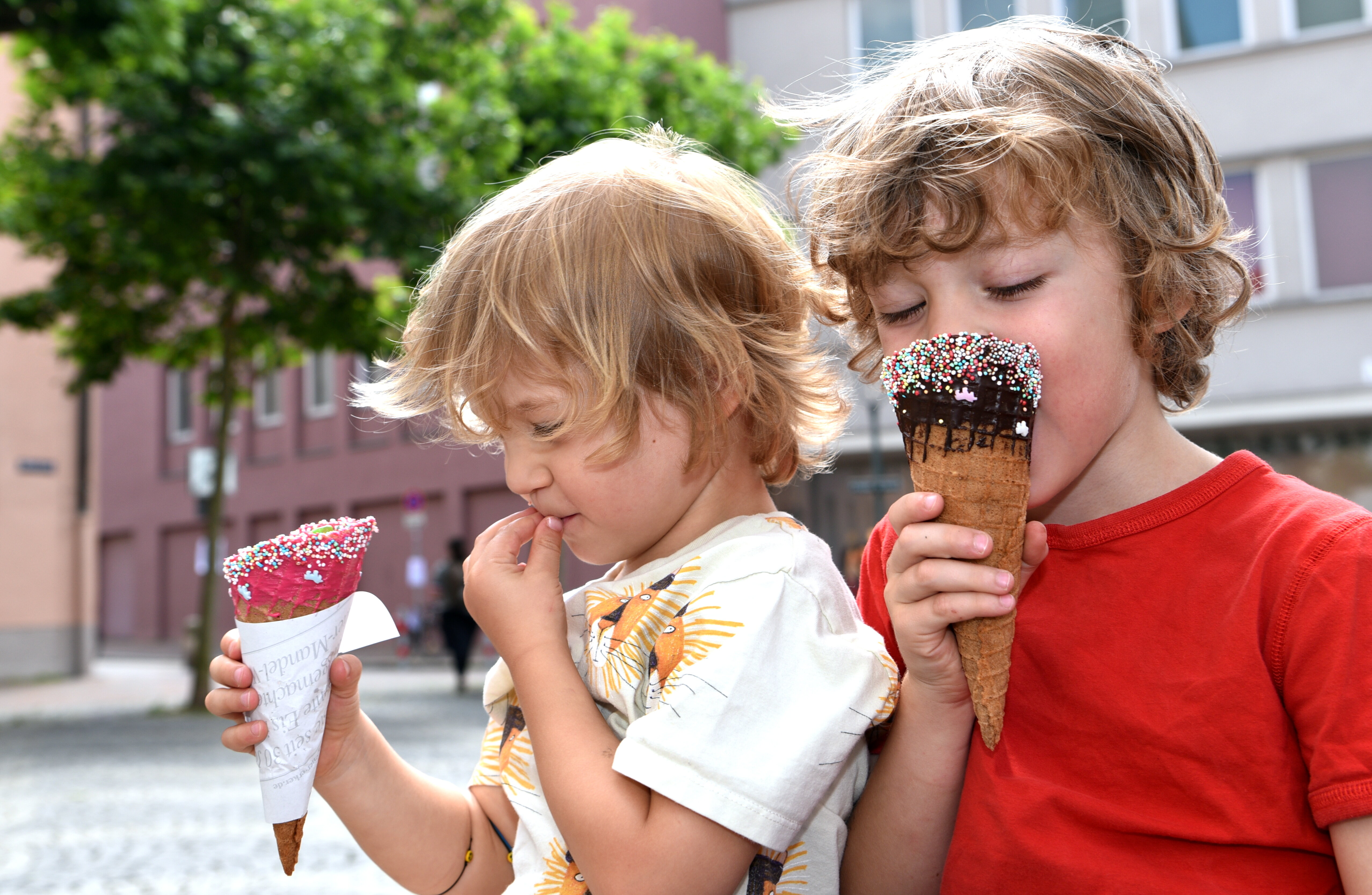2 Kinder essen Eistüten; im Hintergrund ein Baum