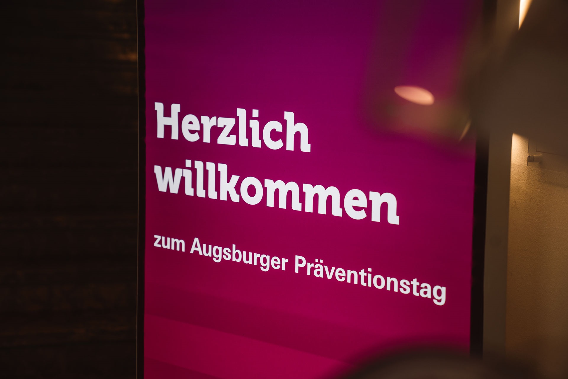 Magentafarbener Aufsteller mit der Aufschrift "Herzlich willkommen zum Augsburger Präventionstag"