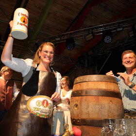 Frau im Dirndl hält einen Bierkrug hoch