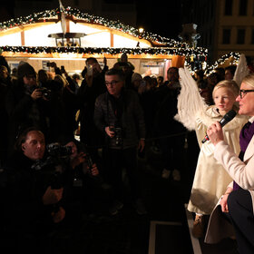 OB Eva Weber und der Weihnachtsengel sprechen in der noch dunklen Budengasse zu Schaulustigen