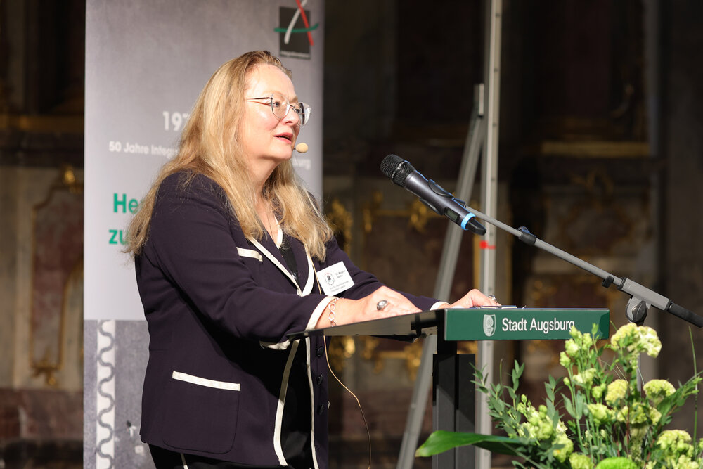 Frau mit langem Haar und Brille am Rednerpult