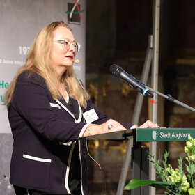 Frau mit langem Haar und Brille am Rednerpult