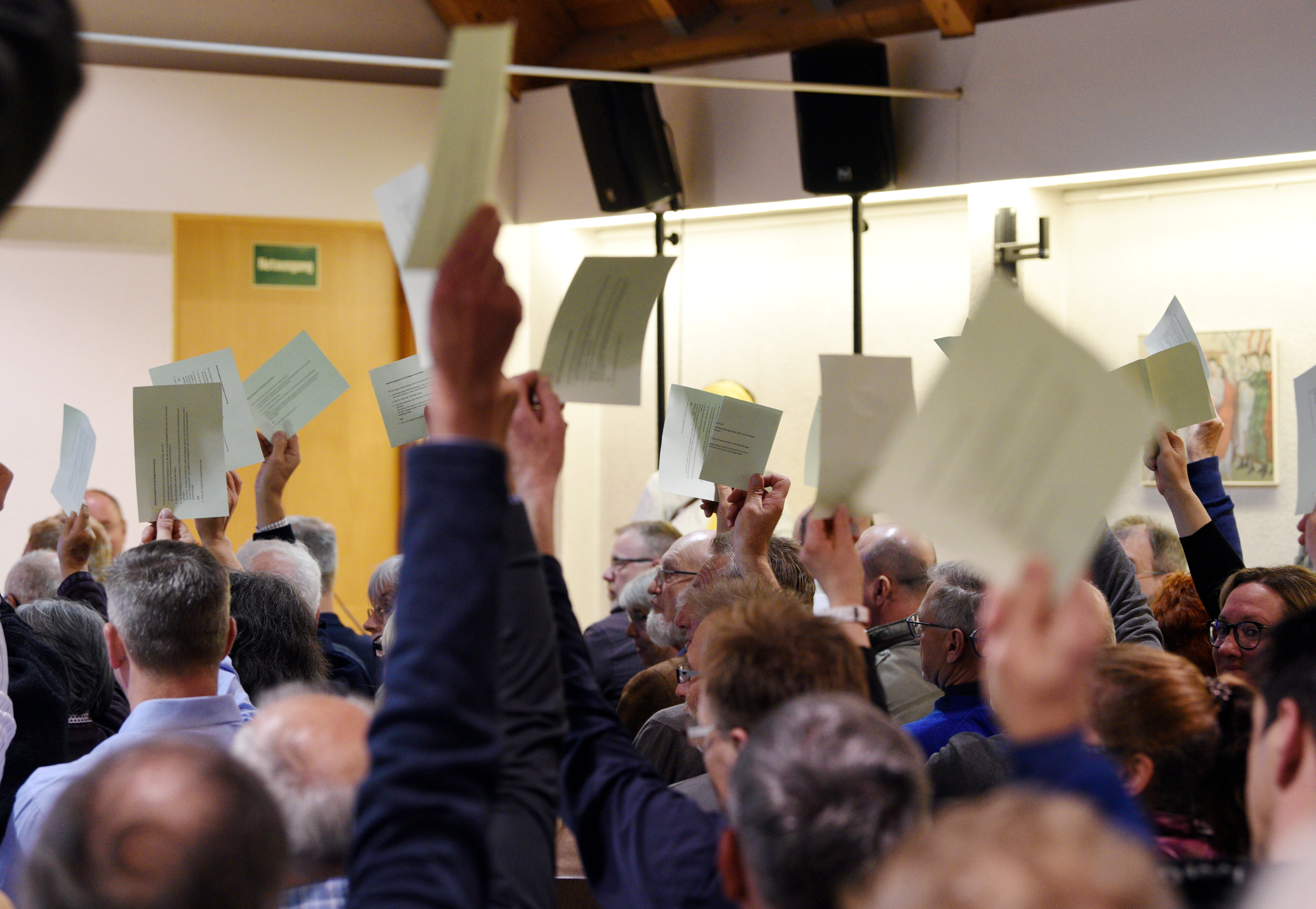 Viele Leute in einem Saal. Sie halten Zettel hoch