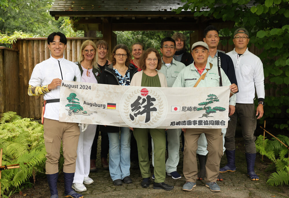 Eine Gruppe von Europäern und Asiaten hält gemeinsam ein Banner, auf dem Augsburg und Amagaski steht