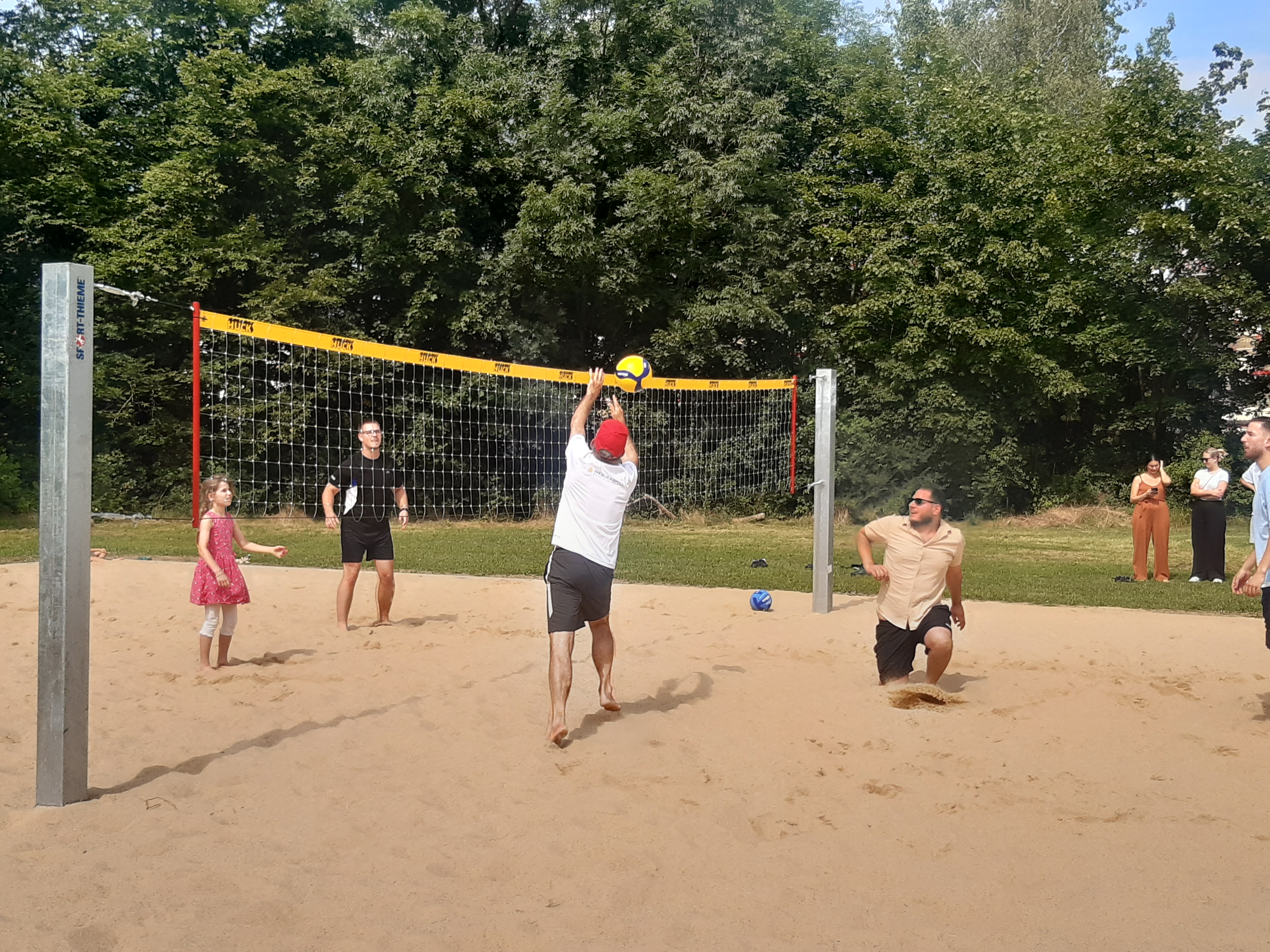 Jugendliche spielen Volleyball auf einem Beachvolleyballfeld. 