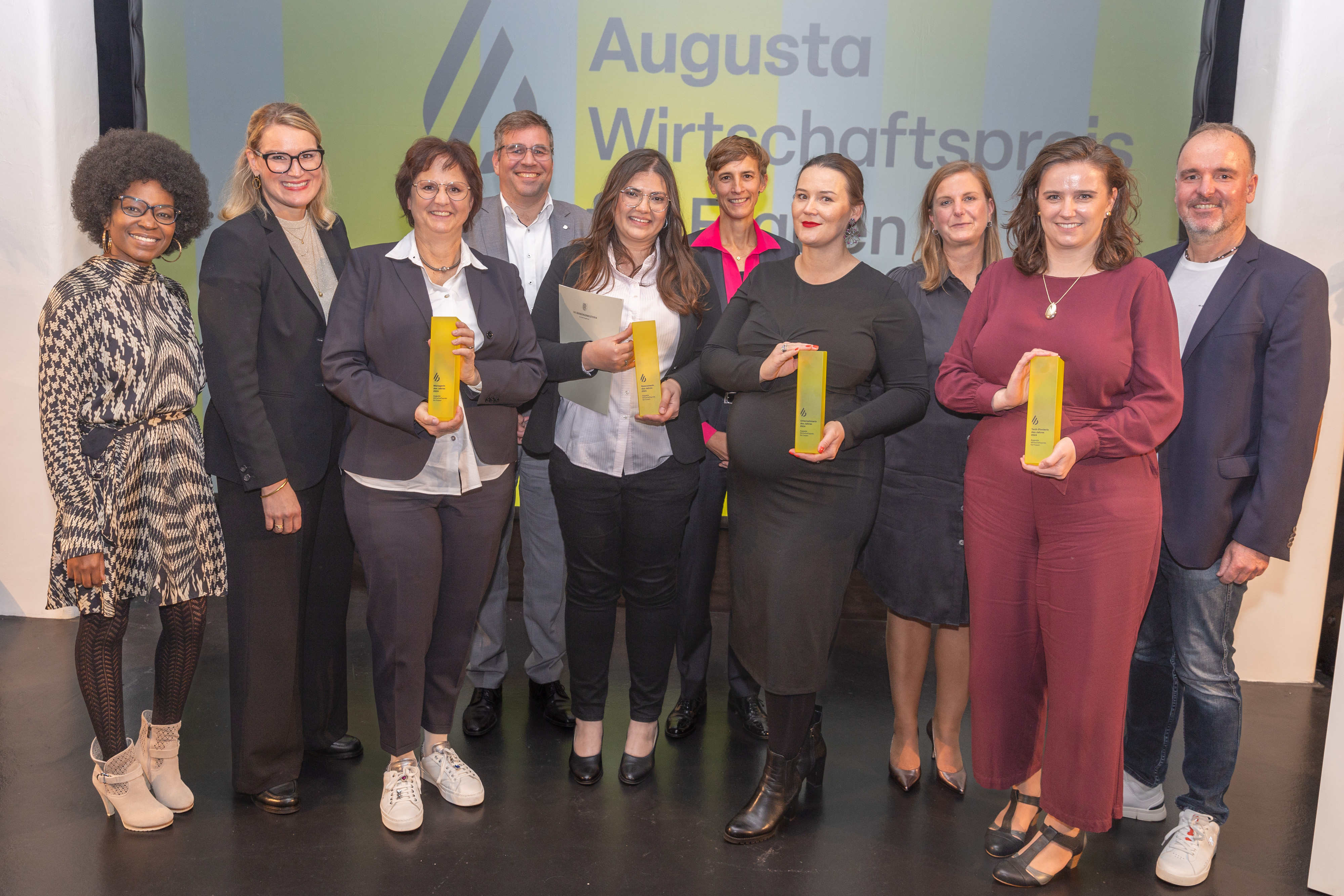 Acht Frauen und zwei Männer in eleganter Kleidung. Vier Frauen halten eine Art Pokal in der Hand