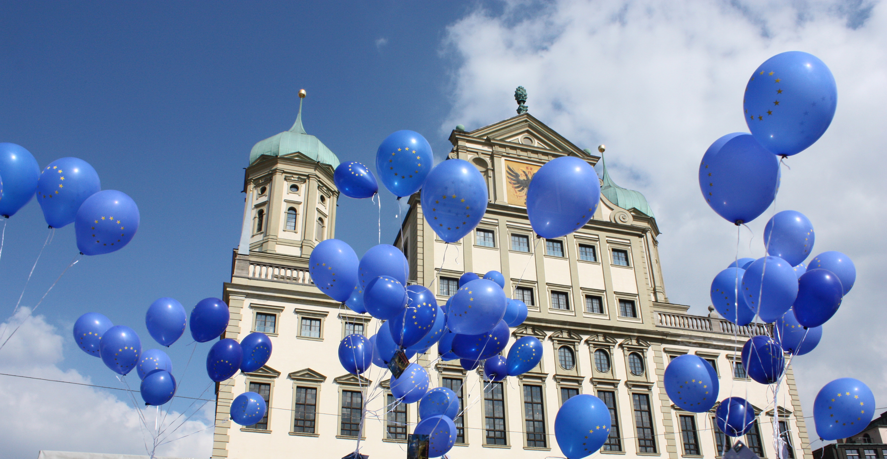 Vor dem Augsburger Rathaus steigen blaue Luftballons mit dem Europa-Logo in den blauen Himmel.