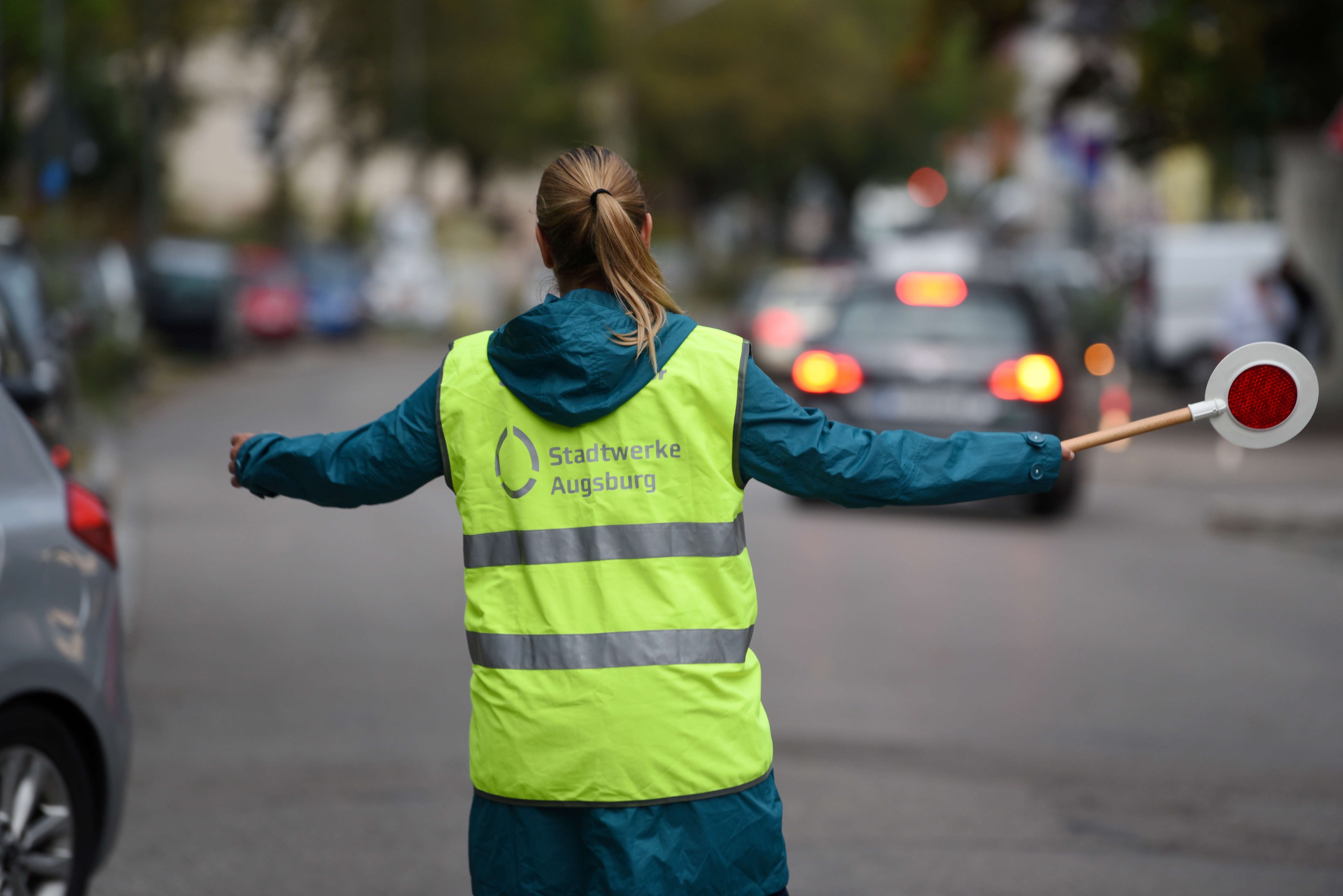 Frau mit Pferdeschwanz, Warnweste und Kelle stoppt den Verkehr