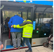 Ein Mensch hilft einem anderen mit Rollator beim Einsteigen in den Bus