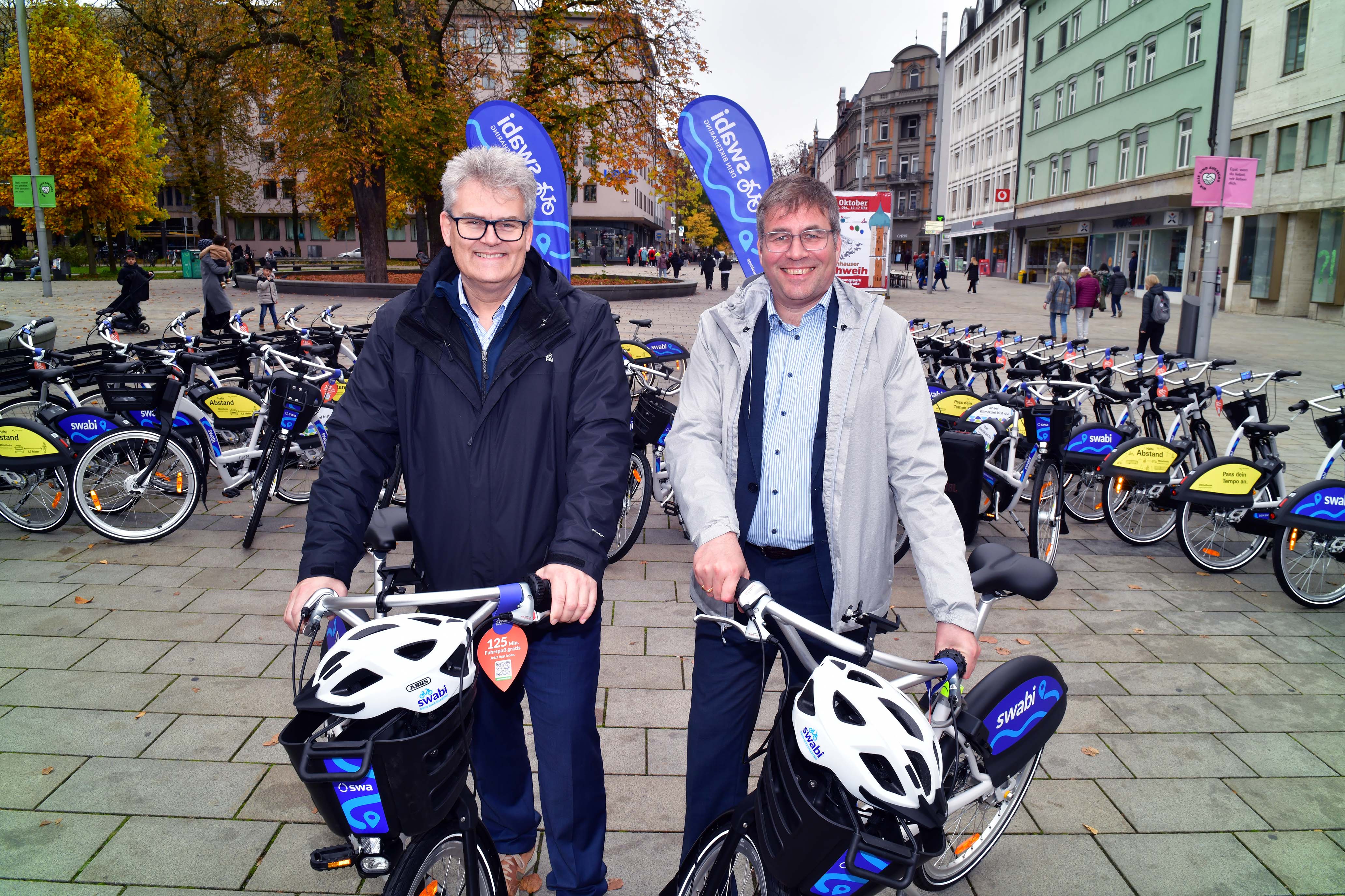 Zwei Männer mit den ersten swabi Bike-Sharing-Rädern. Im Hintergrund sind viele weitere Fahrräder zu sehen.