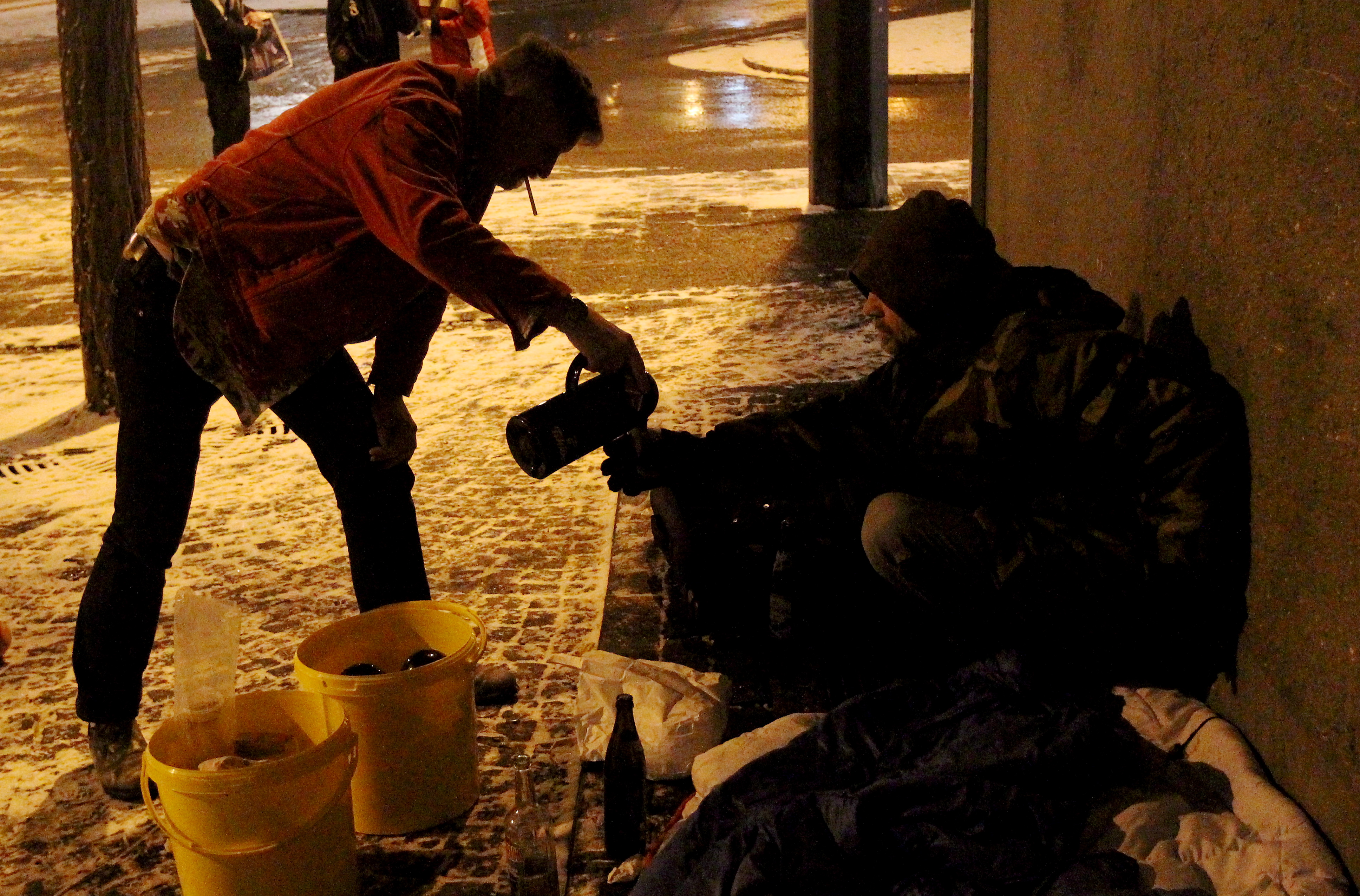 Bei Dunkelheit schenkt ein Mann einem Obdachlosen Tee in einen Becher.