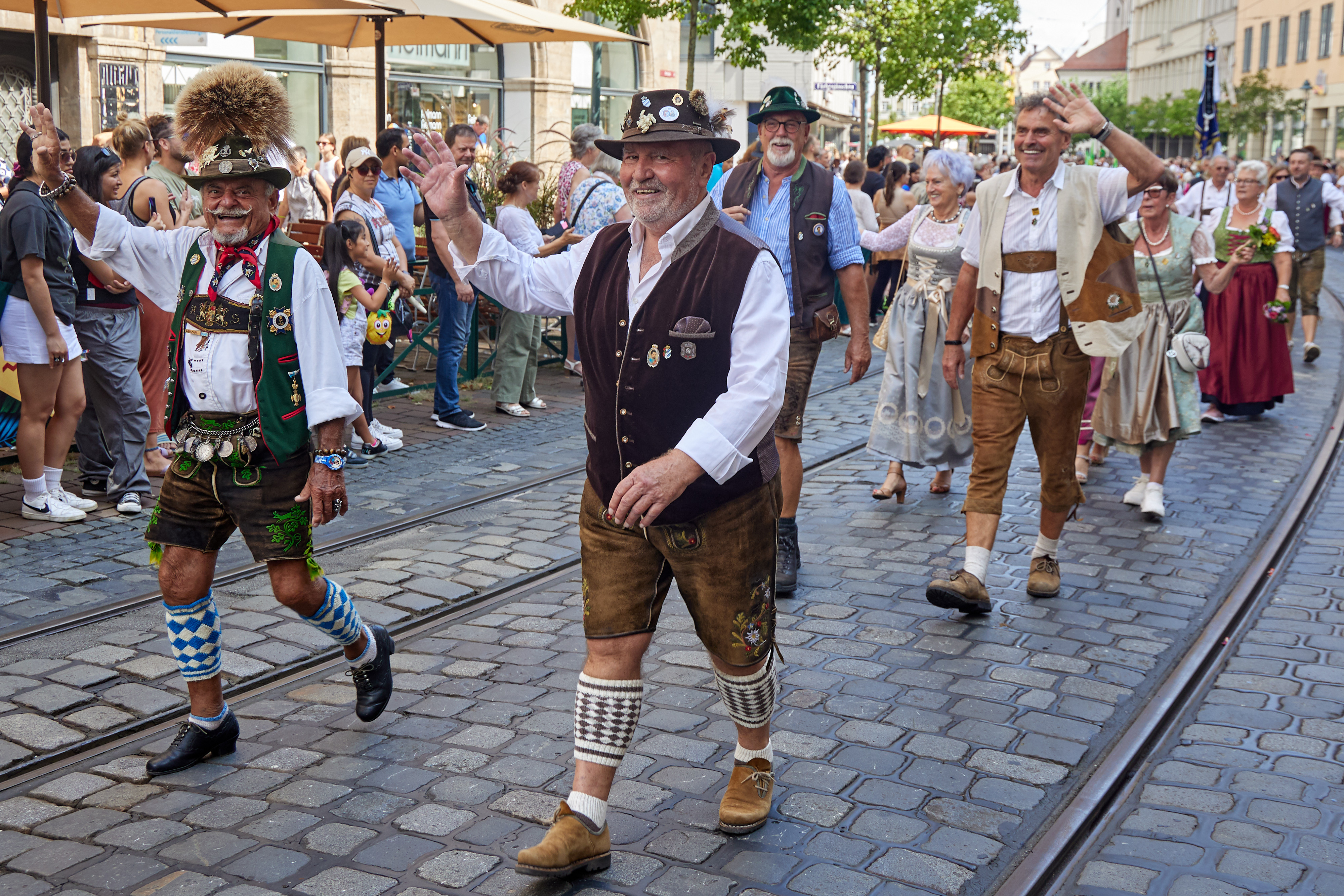 In bayerische Tracht mit Gamsbart am Hut gekleidete Männer winken in die Kamera