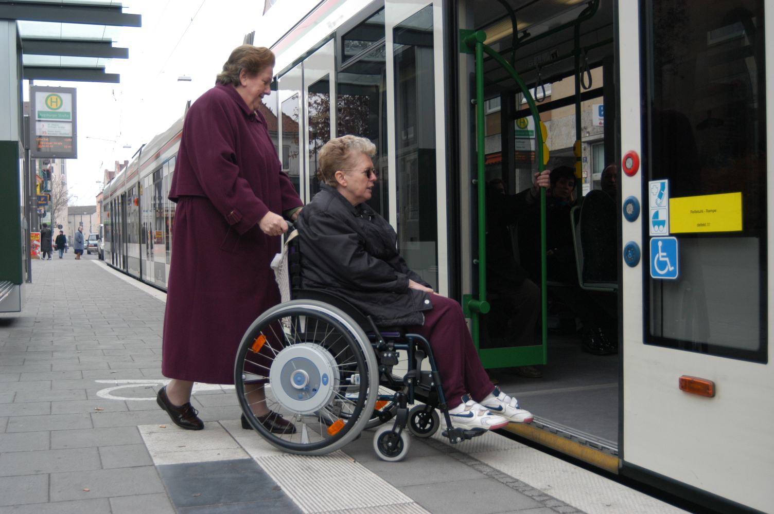 Frau im Rollstuhl wird voon anderer Frau in die Straßenbahn geschoben