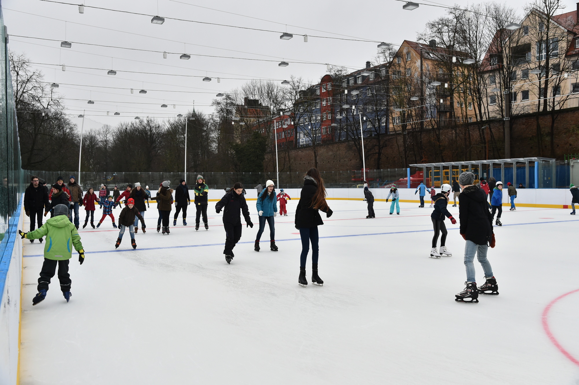Rund 50 Leute beim Schlittschuhlaufen auf einer Eisfläche ohne Dach.