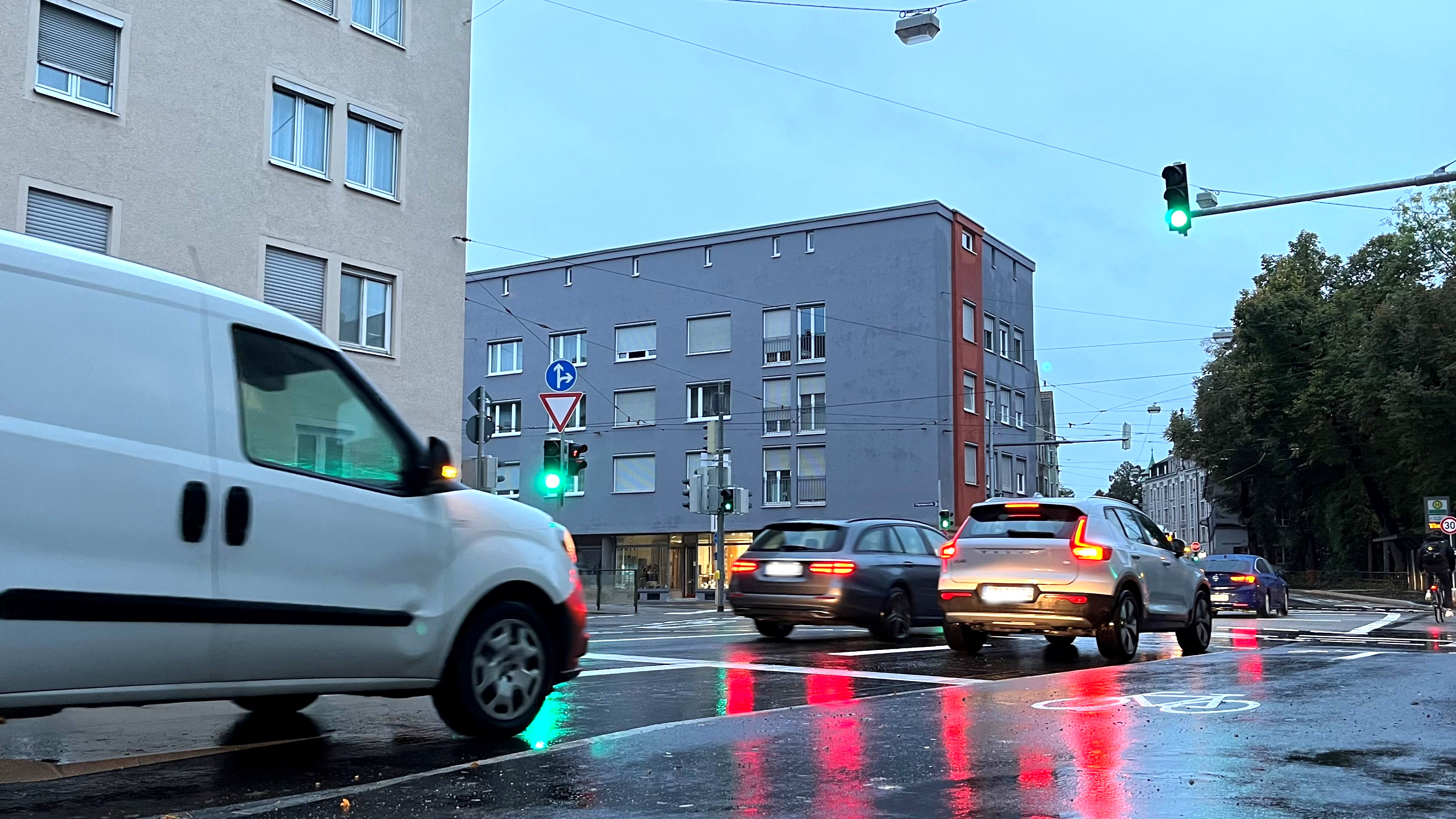 An der Kreuzung Mittlerer Graben und Pilgerhausstraße steht die Ampel auf Grün. Autos und Fahrräder fahren über die Kreuzung. Es herrscht Morgendämmerung, alle Fahrzeuge haben das Licht an.